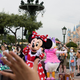 Minnie Mouse points at a camera in front of a crowd of people taking pictures in front of the giant castle structure at Dinsey Shanghai.